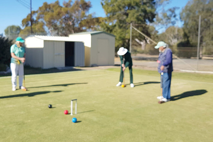 Maureen Lehmann lines up the yellow ball for a shot at the hoop, watched closely by Leanne Combrink and Alec Orcsik.